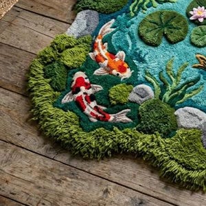 May include: A hand-tufted rug depicting a pond scene with two koi fish, lily pads, and aquatic plants. The rug features a teal blue pond with green and gray accents, and the koi fish are red, white, and orange. The rug is placed on a wooden floor.