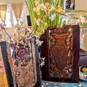 May include: Two antique wooden panels with carved floral and vase designs. One panel features a vase with a rose and other flowers, while the other has a vase with a diamond pattern. The panels are framed in black and brown.
