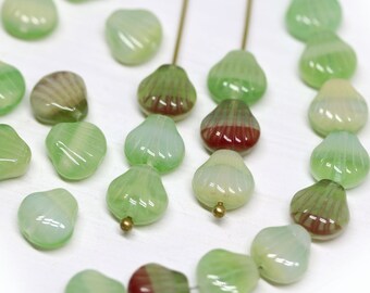 May include: A collection of green and white seashell-shaped glass beads with red accents. The beads are strung on a wire and are ready to be used in jewelry making.