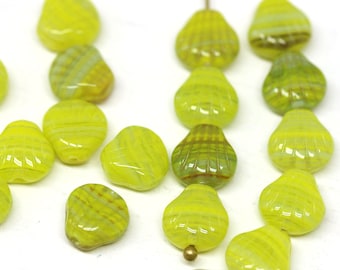 May include: A collection of green and yellow glass beads in the shape of seashells. The beads have a striped pattern and are scattered on a white surface.