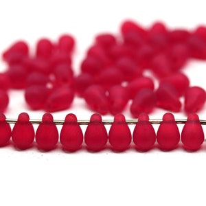 Peut inclure: Un brin de perles de verre rouges en forme de goutte. Les perles sont enfilées sur un fil d'argent.