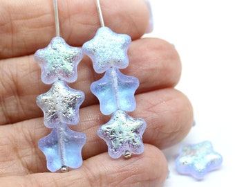 May include: A strand of iridescent blue star-shaped glass beads on a silver wire. The beads are strung in a repeating pattern of three beads. There are also several loose beads in the background.