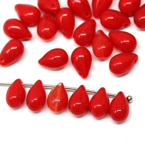 May include: A group of red glass teardrop beads, some are strung on a silver wire. The beads are shiny and have a slight iridescent quality.