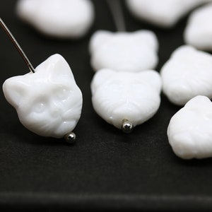 May include: White ceramic cat face beads with a hole for stringing. The beads are smooth and have a glossy finish.