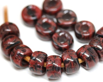 May include: A strand of red and black patterned beads on a brown cord. The beads are round and have a glossy finish.