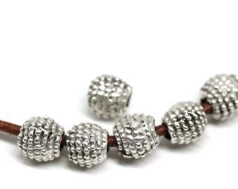 May include: A necklace with silver-coloured, textured beads on a brown leather cord. The beads have a detailed, dotted surface. The jewellery is displayed against a white background, highlighting the design of the necklace.