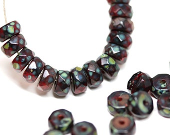 May include: A strand of dark red and teal glass beads with a faceted, geometric design. The beads are strung on a silver wire and are arranged in a semi-circle. There are also several loose beads in the image.