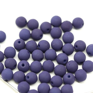 Peut inclure: Un groupe de perles rondes de couleur violet foncé, chacune avec un petit trou au centre. Les perles sont faites d'un matériau mat et ont une surface légèrement texturée.