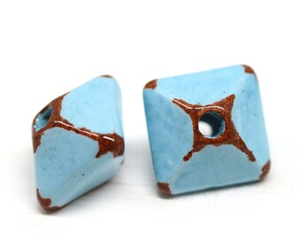 May include: Two light blue ceramic square beads with brown accents and a hole in the center.