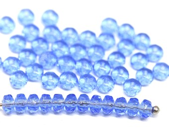 May include: A strand of light blue glass beads with a faceted finish. The beads are strung on a silver wire and are scattered on a white surface.