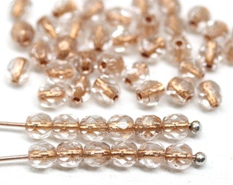 May include: A strand of clear glass beads with a rose gold metallic finish. The beads are faceted and have a slightly irregular shape. The beads are strung on a silver wire.