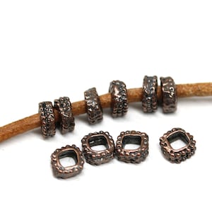 May include: A set of 10 copper-toned metal square spacer beads with a textured surface. The beads have a small hole in the center and are strung on a brown leather cord.