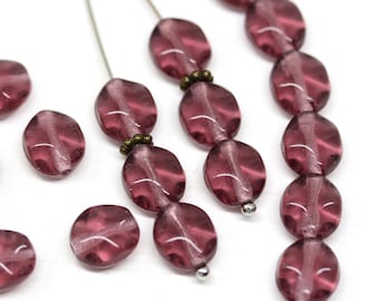 May include: A strand of mauve glass beads with a faceted oval shape. The beads are strung on a silver wire and have a subtle shimmer.