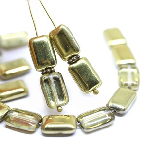 May include: Gold and clear glass rectangular beads with a metallic finish. The beads have a subtle striped pattern and are strung on a wire.
