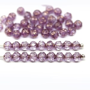 May include: A strand of purple glass beads with a faceted finish. The beads are strung on a silver wire.