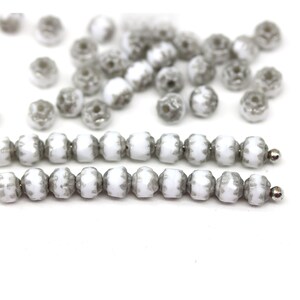 May include: A strand of white glass beads with a grey pattern. The beads are round and have a faceted design.