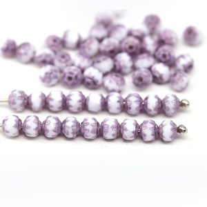 May include: A strand of white and lavender glass beads with a floral pattern. The beads are strung on a silver wire.