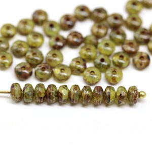 May include: A strand of green glass beads with a brown marbled pattern. The beads are round and have a hole in the centre. The beads are strung on a gold wire.