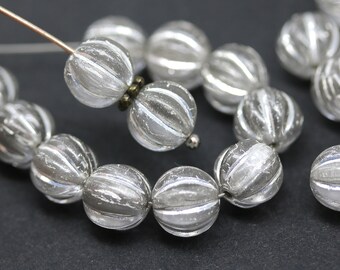 May include: A strand of clear glass beads with silver stripes. The beads are round and have a textured surface.