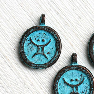 May include: Three round turquoise blue metal pendants featuring a stylised human figure design. The pendants have a dark brown patina and a loop at the top for hanging.