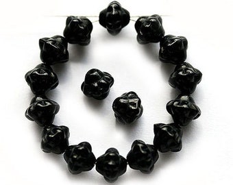May include: A strand of black glass beads with a star-shaped design. The beads are strung on a wire and are arranged in a circle. There are also three loose beads.