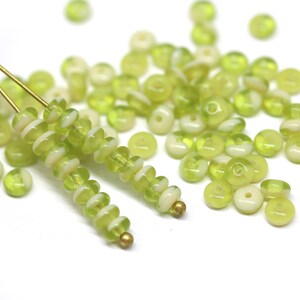 Puede incluir: Una hebra de cuentas de vidrio verde y blanco con un alambre dorado enhebrado. Las cuentas son redondas y tienen un ligero patr&oacute;n de espiral. Tambi&eacute;n hay cuentas sueltas esparcidas alrededor de la hebra.