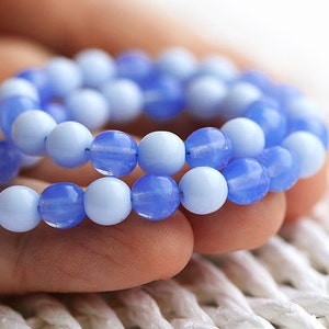 May include: A close-up of a blue and light blue glass bead bracelet. The beads are round and have a smooth, polished finish.