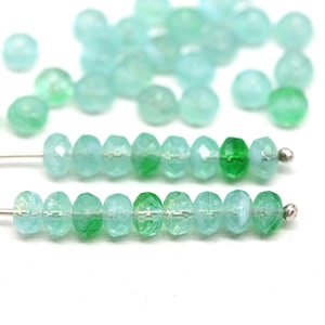 Peut inclure: Gros plan sur des perles rondes et facettées dans des tons de vert et d'aqua. Deux brins de perles sont enfilés sur du fil d'argent, avec des perles en vrac éparpillées en arrière-plan. Les perles ont un aspect étincelant et translucide.