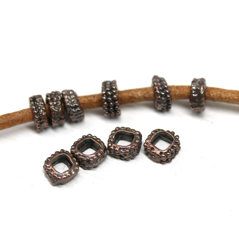 May include: A set of 10 copper-toned metal beads with a square shape and a textured surface. The beads have a small hole in the center for threading.