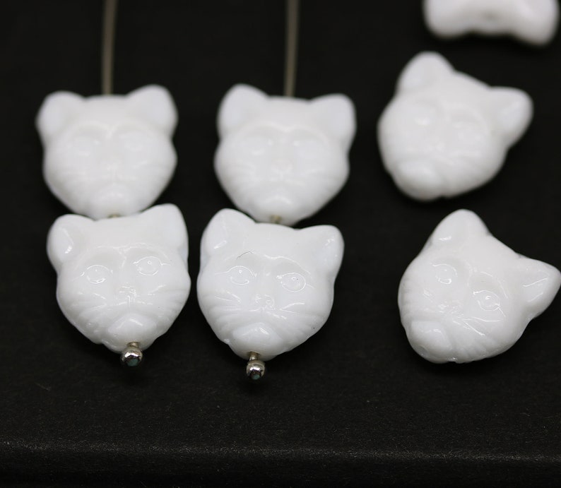 May include: White glass cat head beads with a detailed face and a hole for stringing.