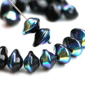 Puede incluir: Una hebra de cuentas de vidrio negro iridiscente con forma de lágrima. Las cuentas tienen un brillo metálico y están enhebradas en un alambre.