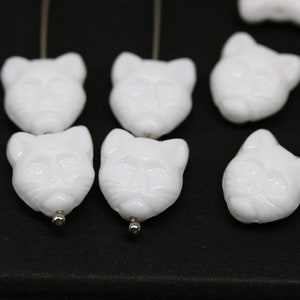 May include: White glass cat head beads with a detailed face and a hole for stringing.