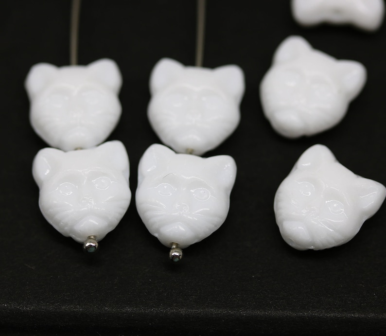 May include: White glass cat head beads with a detailed face and a hole for stringing.