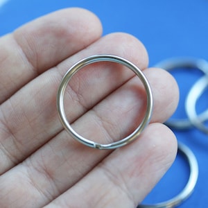 May include: A silver key ring with a circular shape. The ring is held in a hand.
