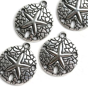May include: Four silver-toned metal charms shaped like sand dollars with a starfish design. Each charm has three holes around the edge.