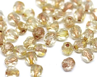 May include: A collection of clear glass beads with gold and copper accents. The beads are faceted and have a slightly irregular shape.
