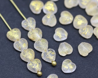May include: A collection of clear glass heart-shaped beads with gold flecks. The beads are strung on a wire and are arranged in a row. The beads are on a black surface.