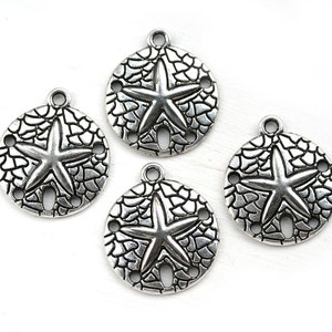 May include: Four silver-toned metal charms shaped like sand dollars with a starfish design in the center. Each charm has three holes around the edge.
