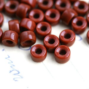 May include: A group of small, round, terracotta-colored ceramic beads with a hole in the center. The beads are scattered on a white surface.