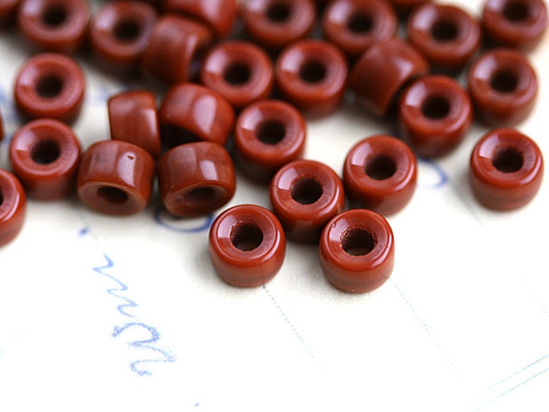 May include: A group of small, round, terracotta-colored ceramic beads with a hole in the center. The beads are scattered on a white surface.