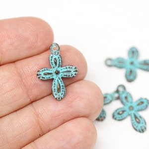 May include: A set of four turquoise blue metal cross charms with an ornate design. The charms have a loop at the top for attaching to jewelry or other crafts.