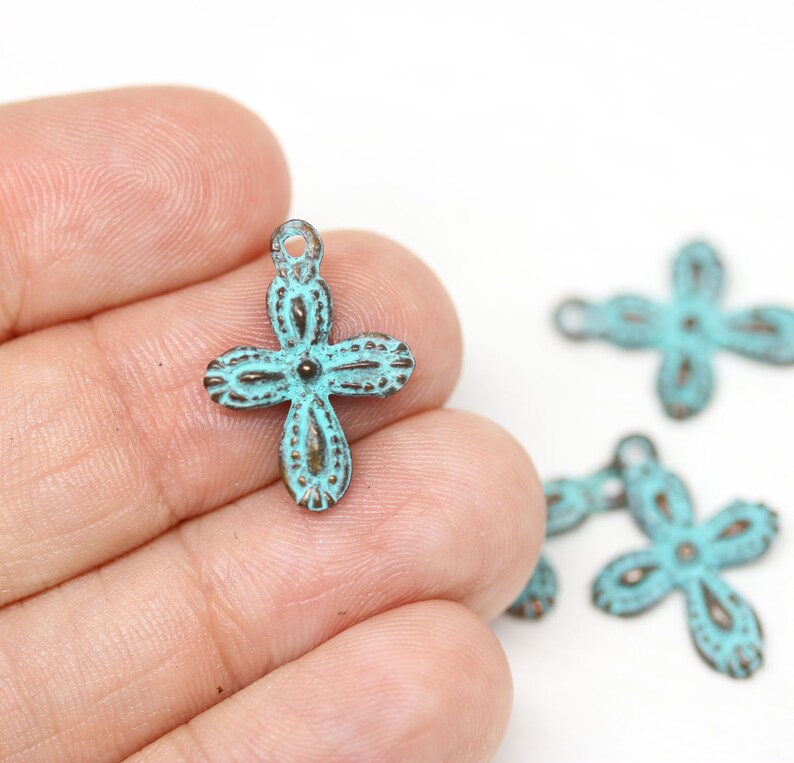 May include: A set of four turquoise blue metal cross charms with an ornate design. The charms have a loop at the top for attaching to jewelry or other crafts.