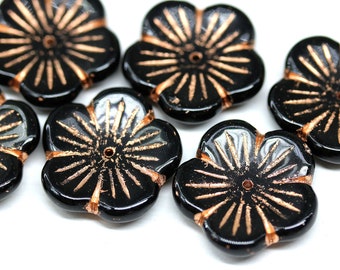 May include: Six black glass flower-shaped beads with a copper-colored design. The beads have a hole in the center for stringing.