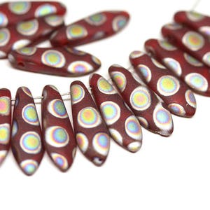 May include: A strand of red glass beads with white and iridescent circles. The beads are shaped like teardrops and have a glossy finish.