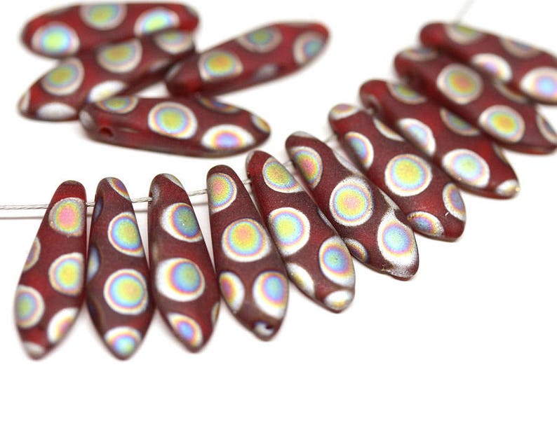 May include: A strand of red glass beads with white and iridescent circles. The beads are shaped like teardrops and have a glossy finish.