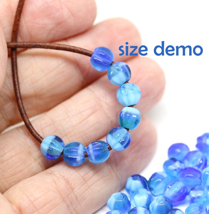 Peut inclure: Un fil de perles de verre bleues et blanches sur un cordon marron. Les perles sont rondes et stri&eacute;es. Le texte "size demo" est visible. Un tas de perles similaires est dans le coin inf&eacute;rieur droit.