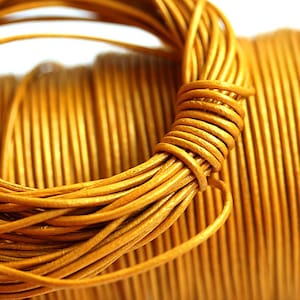 Könnte beinhalten: Nahaufnahme einer Spule aus goldgelbem Lederband. Das Band ist eng gewickelt und zeigt eine detaillierte Textur. Das Bild hebt die Farbe des Bandes und die Art und Weise, wie es aufgerollt ist, hervor, was auf seine Verwendung in der Herstellung oder Schmuckherstellung hindeutet.