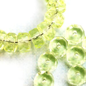 May include: A strand of light green faceted glass beads, with a few loose beads scattered around. The beads are all round and have a smooth, polished finish.