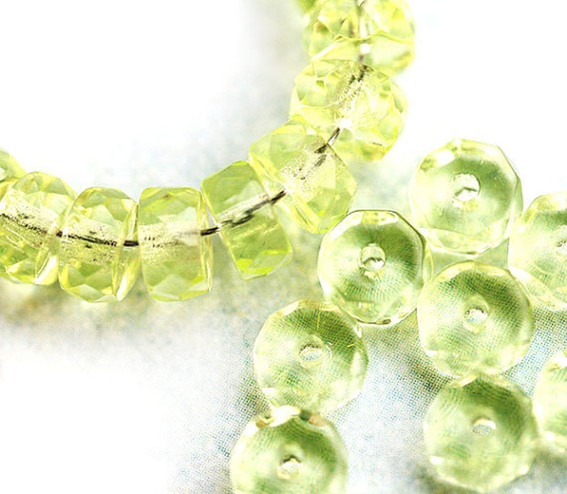 May include: A strand of light green faceted glass beads, with a few loose beads scattered around. The beads are all round and have a smooth, polished finish.