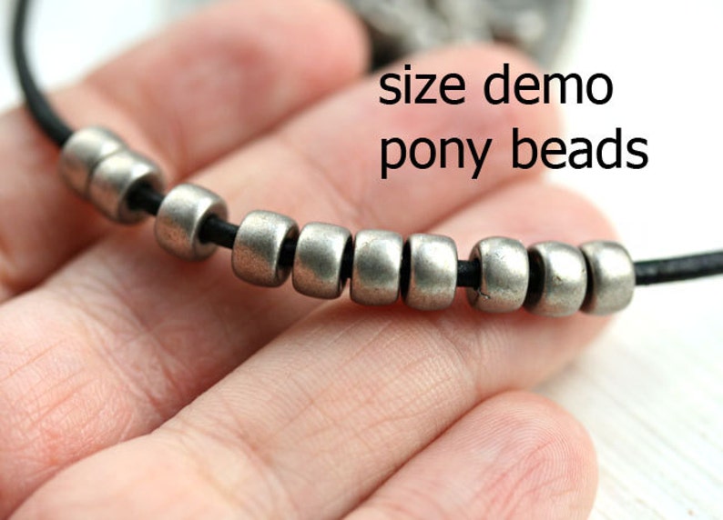 May include: Close-up of a silver pony bead necklace on a black cord. The beads are small and round, and the cord is thin. The text "size demo pony beads" is visible in the image.